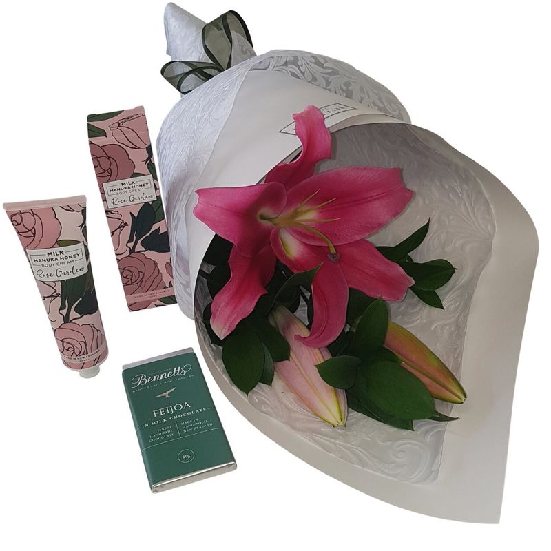 pink%20lily%20wrapped%20in%20white%20embossed%20paper%20cone%2C%20pink%20rose%20handcream%20and%20bennetts%20of%20mangawhai%20feijoada%20chocolate.%20There%20is%20a%20green%20ribbon%20on%20the%20flowers., 