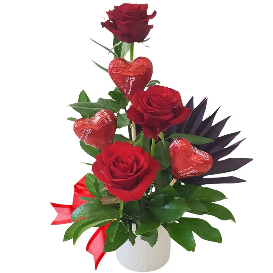 Arrangement of red roses in ceramic vase with chocolate hearts