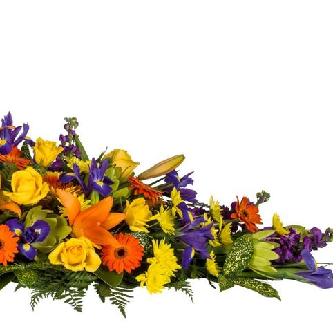 Bright Life Casket Spray side view bright casket spray flowers. Purple Iris, orange lilies, orange gerberas, yellow roses, foliages.