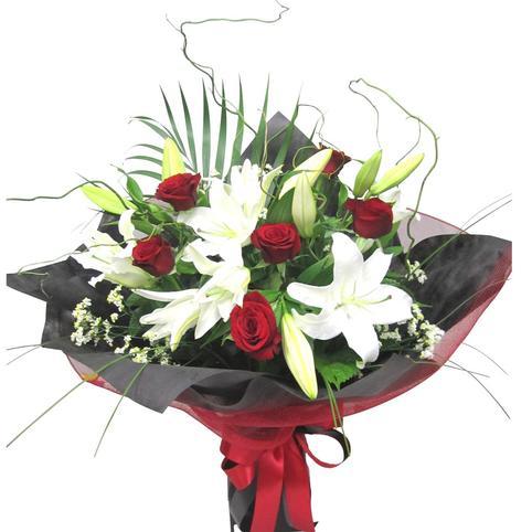 red roses and white lilies with some lilies open and some in bud. With palm, twigs in stylish black and red wrapping.