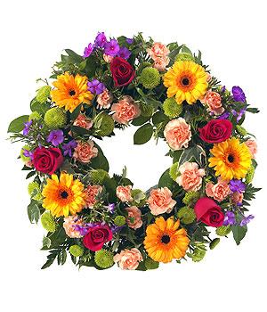 Bright colourful wreath. Assorted bloom design of seasonal colourful flowers. Gerberas, roses, freesias, carnations leaves in wreath.