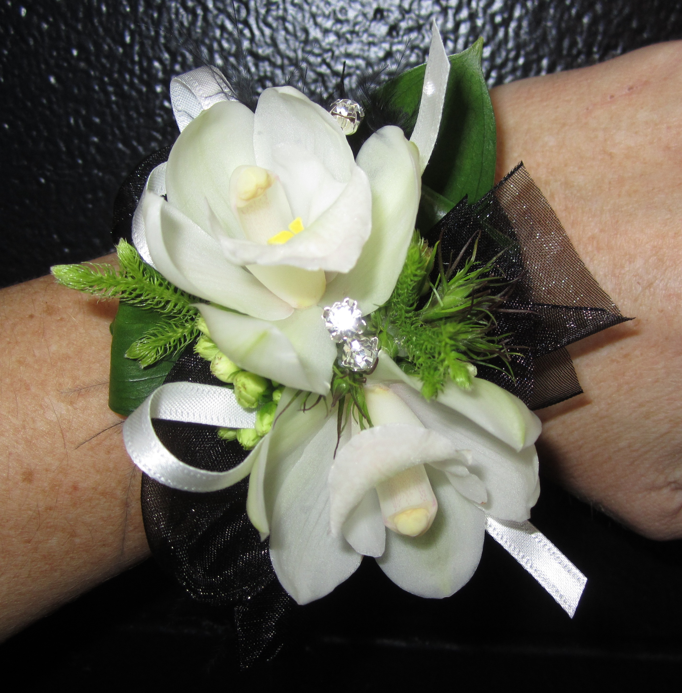 Photo of white orchid corsage with ribbon and decorations.